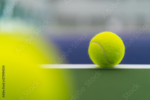one new tennis ball on white line in blue and green hard court with blurred ball on left foreground © angyim