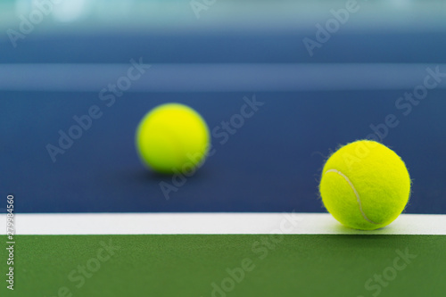 one new tennis ball on white line in blue and green hard court with blurred ball on left © angyim