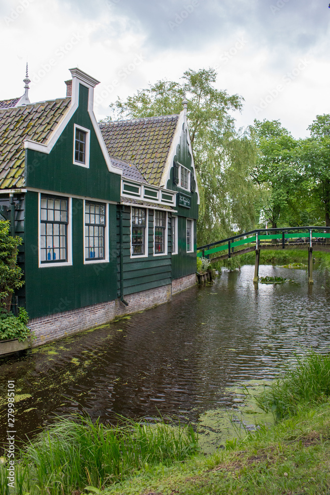 Obraz premium Wooden rural buildings with wooden bridge and trees. Idyllic countryside landscape. Beautiful houses near canal. Old buildings in Europe. Village landscape. Historical village in Europe.