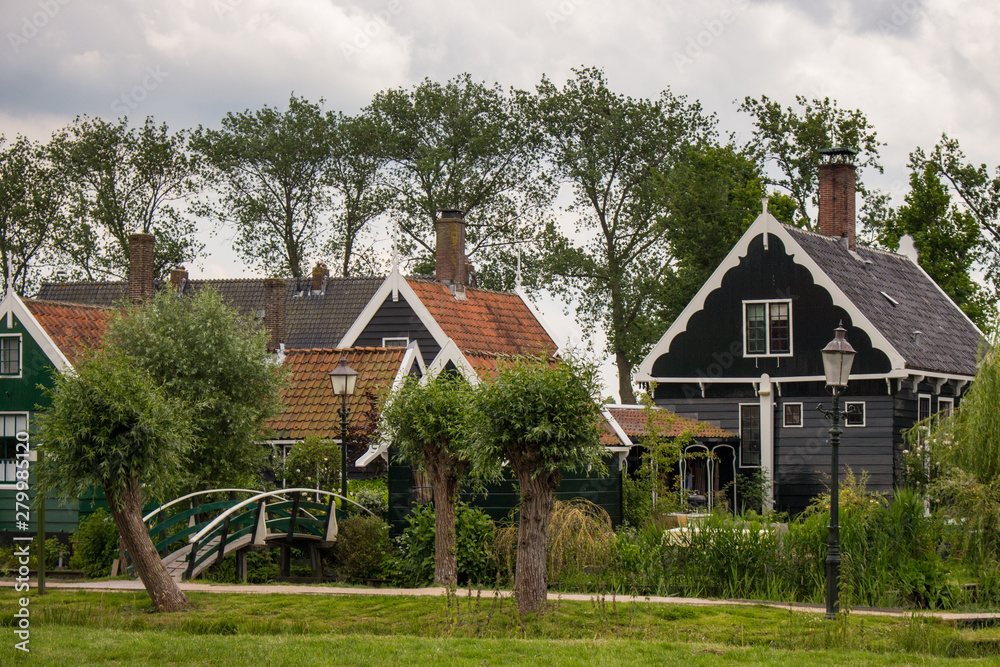 Pretty rural buildings with wooden bridge and trees. Idyllic countryside landscape. Typical holland houses with vintage bridge over river. Old buildings in Zaanse Schans, Netherlands. 