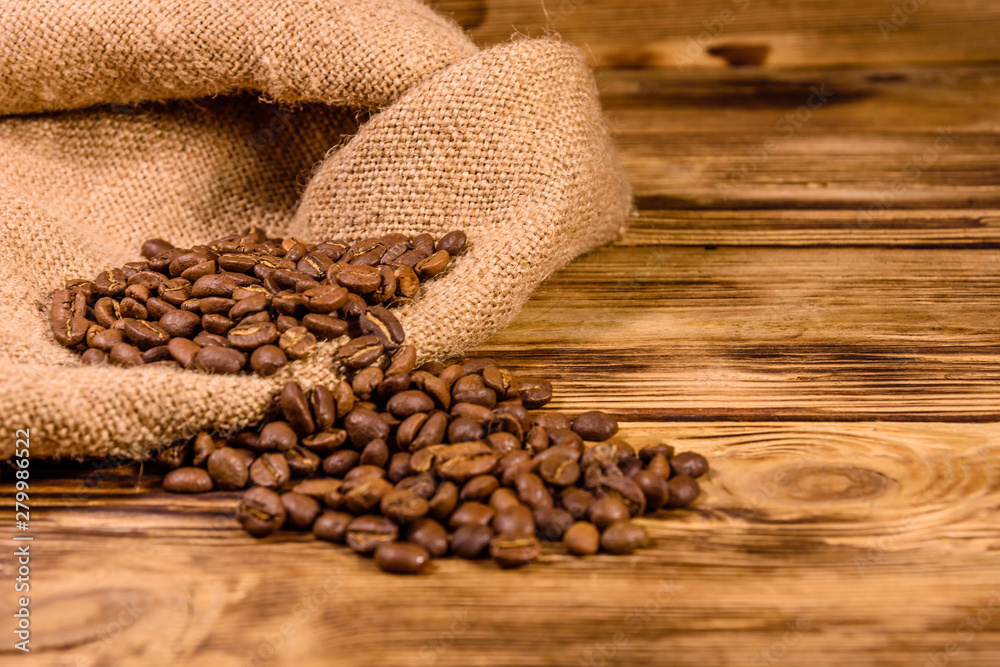 Sackcloth and scattered coffee beans on wooden table Sackcloth and scattered coffee beans on wooden table