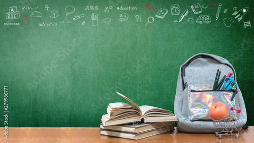 Back to school concept with school books, textbooks, backpack and stationery supplies on classroom desk with teacher's green chalkboard background with educational doodle for new academic year begin
