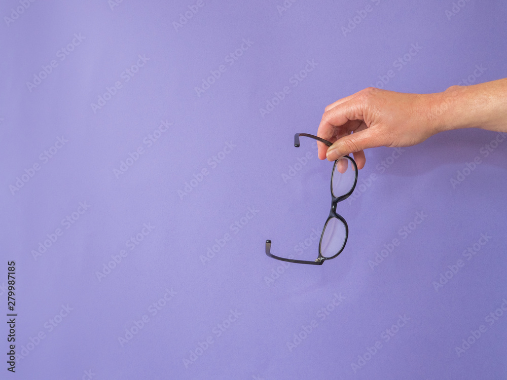 Hand with glasses on purple background with copy space