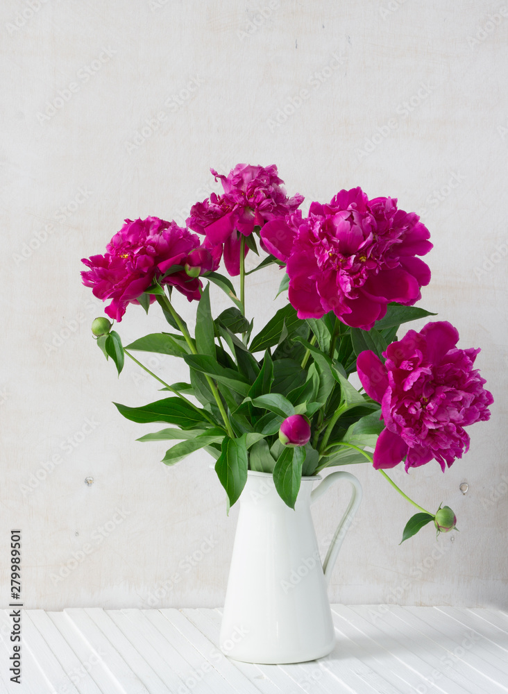 Purple garden peonies in a white enamel jug on a white wooden background, rustic style Purple garden peonies in a white enamel jug on a white wooden background, rustic style