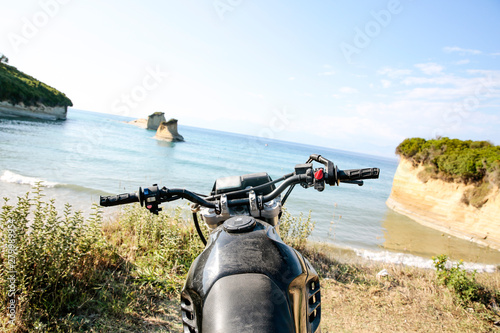 A motorcycle on the sandy cliff on the blue sky and ocean view in distance.