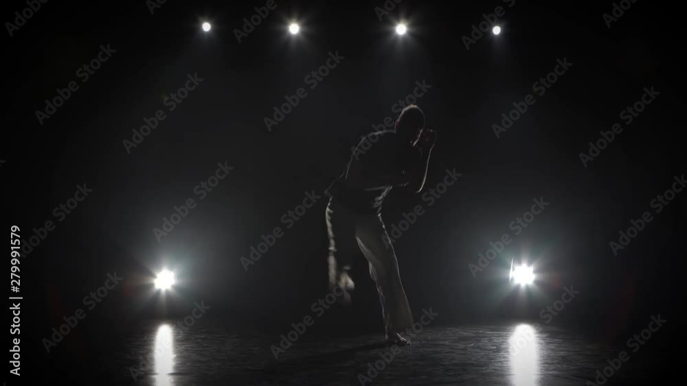 Strong man practicing capoeira in darkness against spotlight in studio. Strong man practicing capoeira in darkness against spotlight in studio.