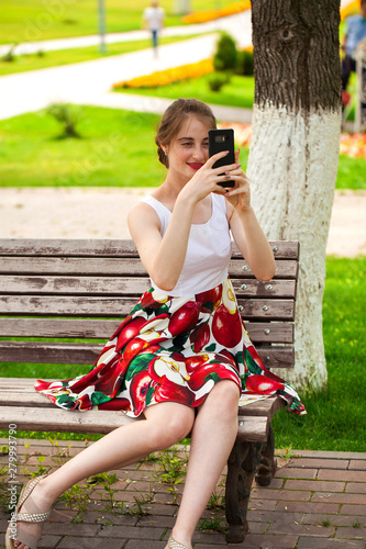 Calling by phone. Beautiful girl in summer dress sitting on a park bench © Andrey_Arkusha