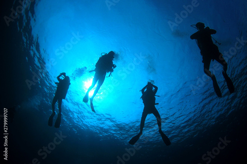 Scuba divers hover at safety stop. Silhouette against sun 