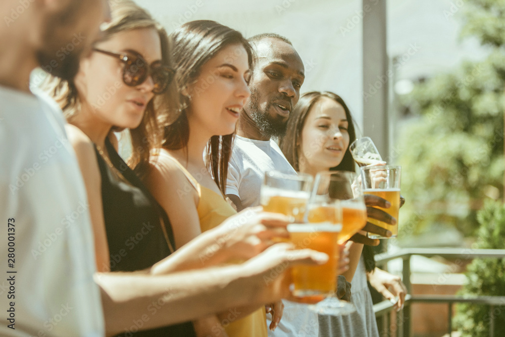 Young group of friends drinking beer, having fun, laughting and celebrating together. Women and men with beer's glasses in sunny day. Oktoberfest, friendship, togetherness, happiness, summer concept. Young group of friends drinking beer, having fun, laughting and celebrating together. Women and men with beer's glasses in sunny day. Oktoberfest, friendship, togetherness, happiness, summer concept.