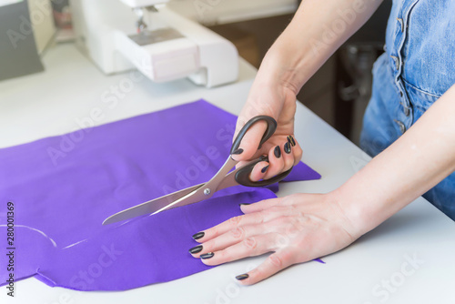 pattern, scissors, tape measure, and a sewing machine. Workplace of seamstress. Dressmaker cuts dress detail on the sketch lines.