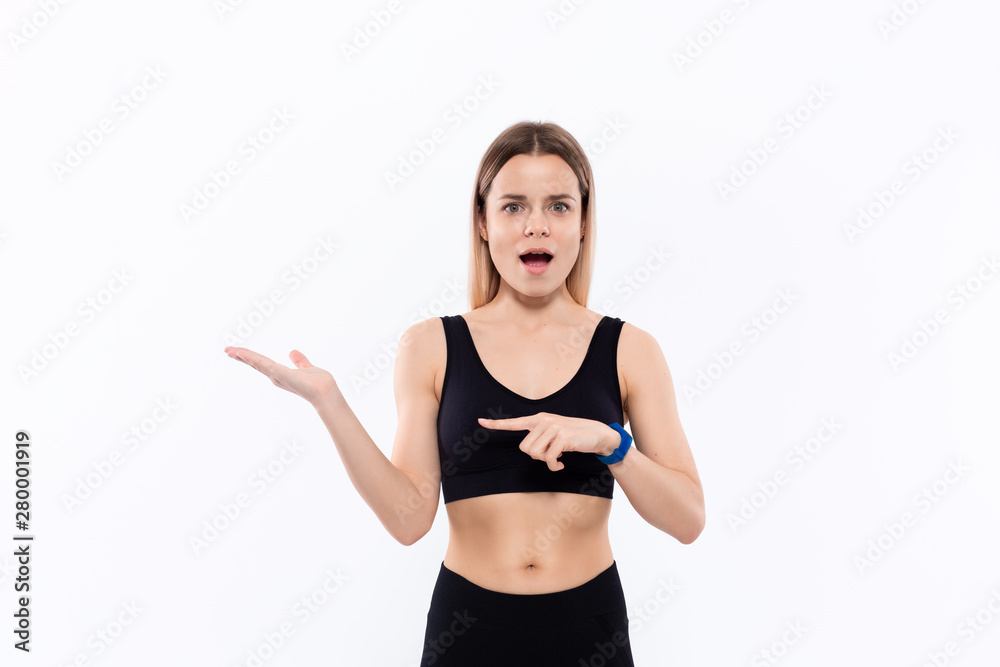 Young sporty blond woman in a black sportswear with smart watches for pulse measuring pointing with one hand at the pulm of a hand