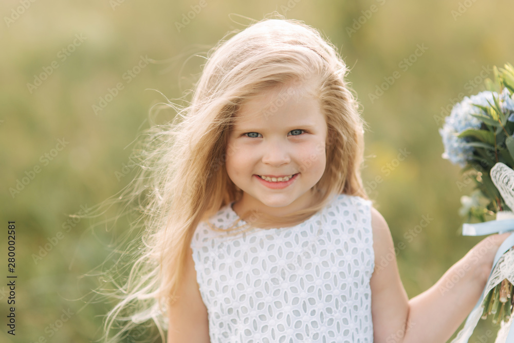 Portrait of beautiful little blond hair girl in field. Girl stand in front of big tree and hold bouquet of flowers Portrait of beautiful little blond hair girl in field. Girl stand in front of big tree and hold bouquet of flowers