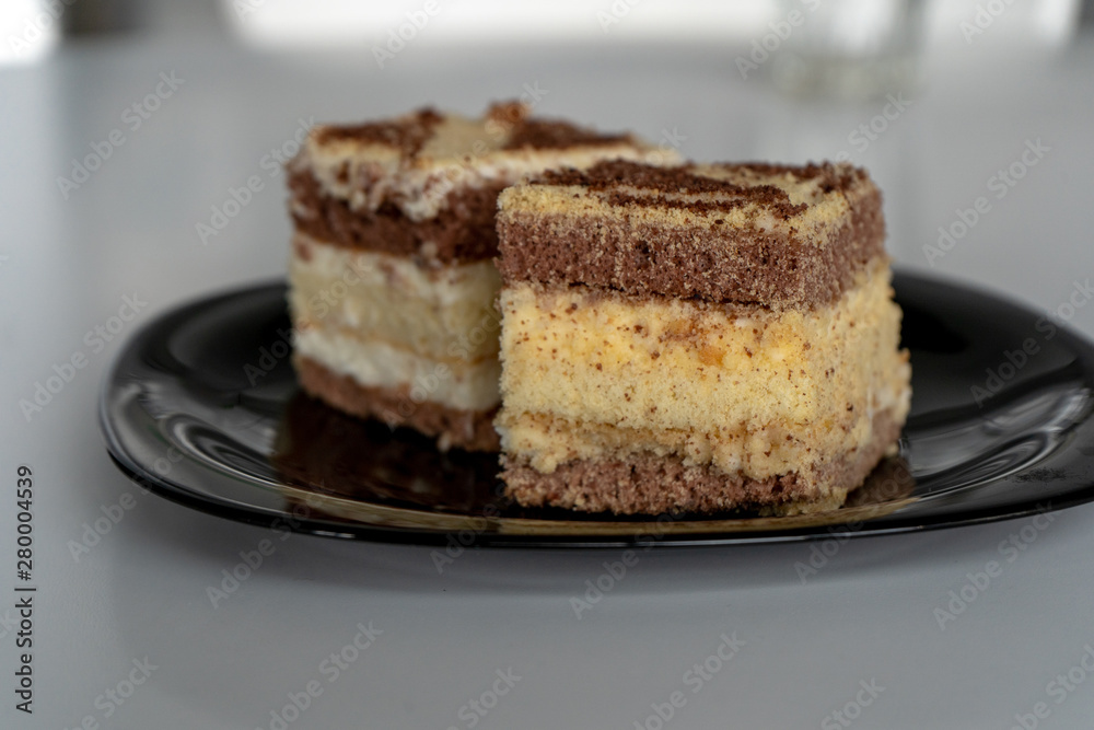 Two pieces of homemade chocolate sponge cake with cream on a black plate on a white table in the kitchen. Side view