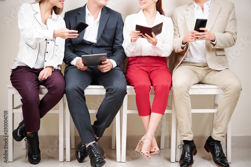 Close-up of young businessmen and businesswomen sitting on chairs and using their gadgets tablet pc and mobile phone
