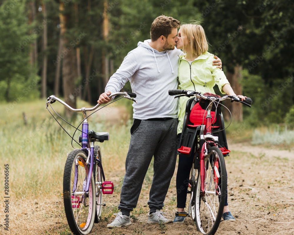 Fototapeta premium Couple kissing next to bikes on forest road