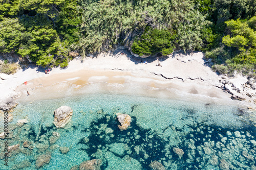 Aerial view of green seashore and turquoise sea water. Island with green trees in the ocean seen form above.