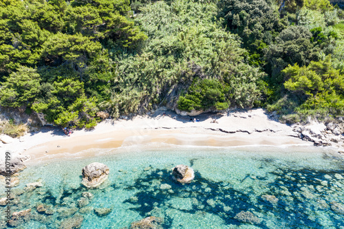 Aerial view of green seashore and turquoise sea water. Island with green trees in the ocean seen form above.