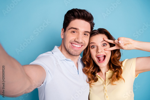 Close up photo of foxy lady brunet guy pair making selfies v-sign symbol near eye wear casual t-shirts isolated blue background