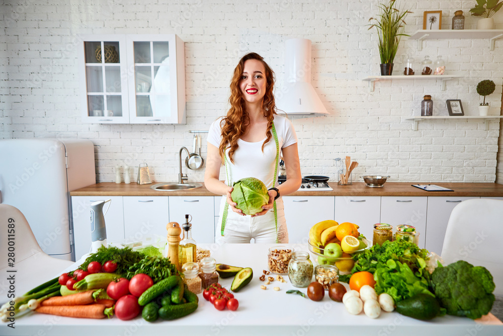 Young happy woman holding cabbage in the beautiful kitchen with green fresh ingredients indoors. Healthy food and Dieting concept. Loosing Weight