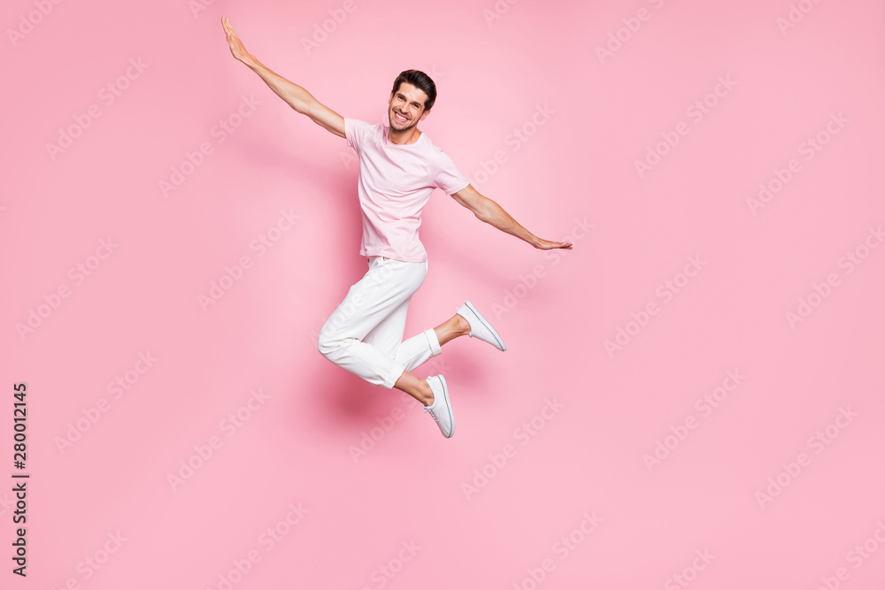 Full length photo of handsome man raising hands arms smiling jumping wearing white t-shirt pants trousers isolated over pink background Full length photo of handsome man raising hands arms smiling jumping wearing white t-shirt pants trousers isolated over pink background