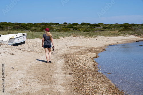 Fototapeta Naklejka Na Ścianę i Meble -  Women walking alongside an empty beach in Sardinia looking at a boat wreck lying at the waterside