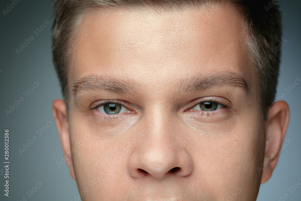 Close-up portrait of young man isolated on grey studio background. Caucasian male model looking at camera and posing, looks serious. Concept of men's health and beauty, self-care, body and skin care. Close-up portrait of young man isolated on grey studio background. Caucasian male model looking at camera and posing, looks serious. Concept of men's health and beauty, self-care, body and skin care.