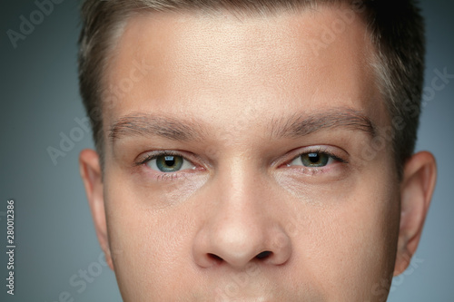 Close-up portrait of young man isolated on grey studio background. Caucasian male model looking at camera and posing, looks serious. Concept of men's health and beauty, self-care, body and skin care.