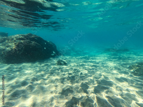 Underwater view of the rocks, sand and stones. The sandy and rocky bottom of the sea with some sun rays. © magdal3na