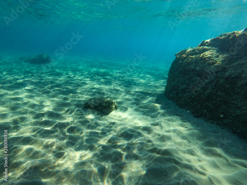 Underwater view of the rocks, sand and stones. The sandy and rocky bottom of the sea with some sun rays.