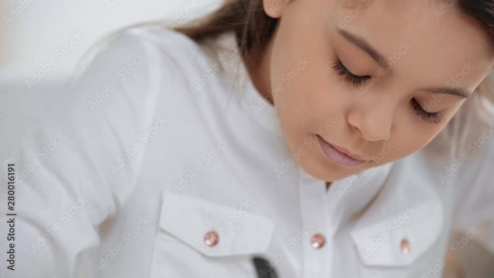 focused schoolgirl in white shirt blinking while writing in copy book focused schoolgirl in white shirt blinking while writing in copy book