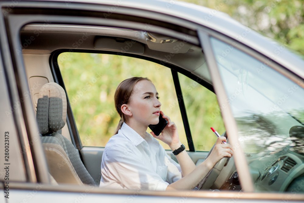 Picture of young businesswoman speaks by phone and doing makeup while driving a car in the traffic jam