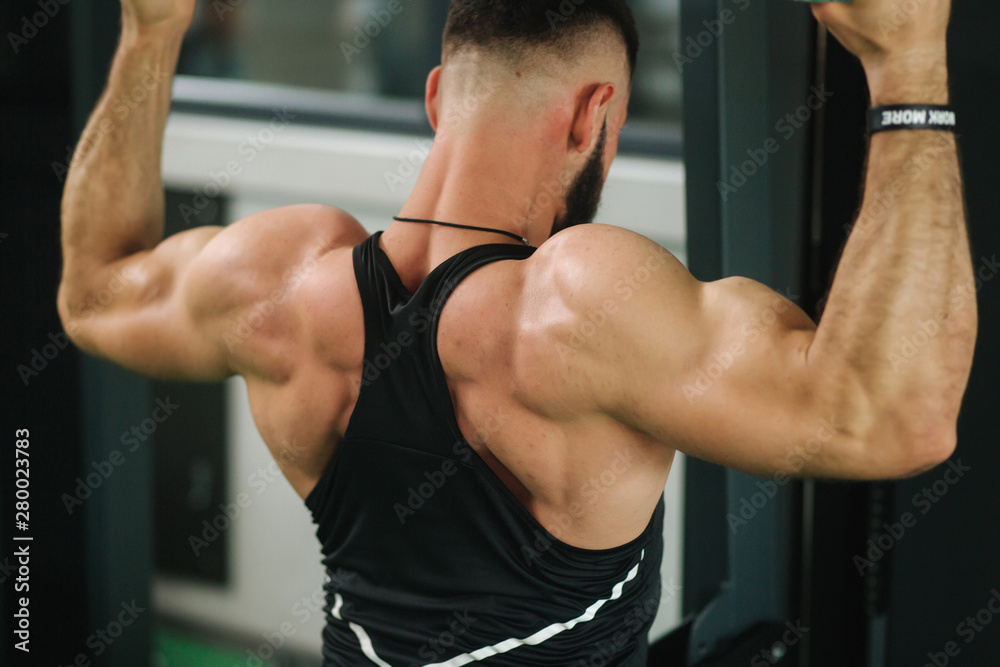 A young athlete trains in the gym. Shows the muscles of the back and chest. Back view A young athlete trains in the gym. Shows the muscles of the back and chest. Back view