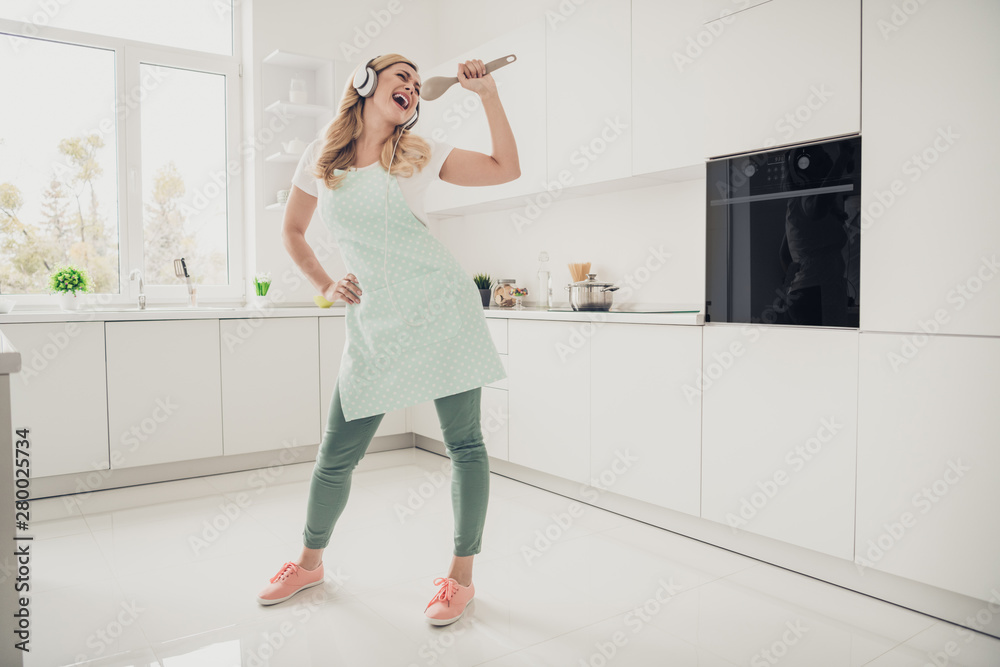 Full length body size view portrait of her she nice attractive lovely cheerful cheery carefree wavy-haired lady having fun singing karaoke in light white interior kitchen Full length body size view portrait of her she nice attractive lovely cheerful cheery carefree wavy-haired lady having fun singing karaoke in light white interior kitchen