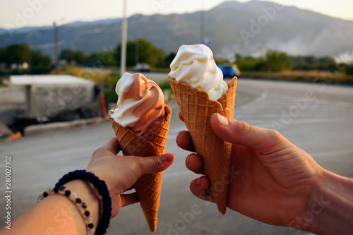 A couple or friends are holding an ice cream cones in their hands outdoor. Summer road trip snack break. 