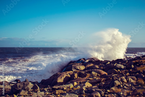 Stormy sea with big waves splashing against the black volcanic rocks in Southeast Iceland near Höfn. The sunny day with a clear sky.  