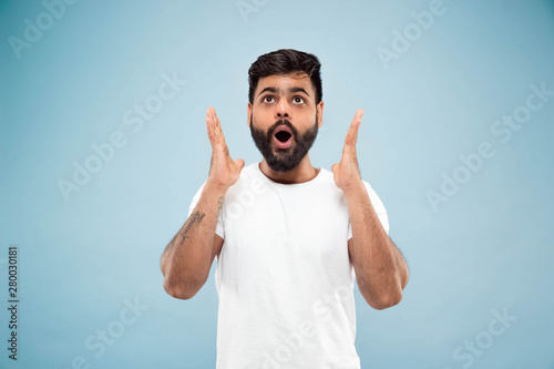 Half-length close up portrait of young hindoo man in white shirt on blue background. Human emotions, facial expression, ad concept. Negative space. Shocked, astonished or crazy happy feelings.