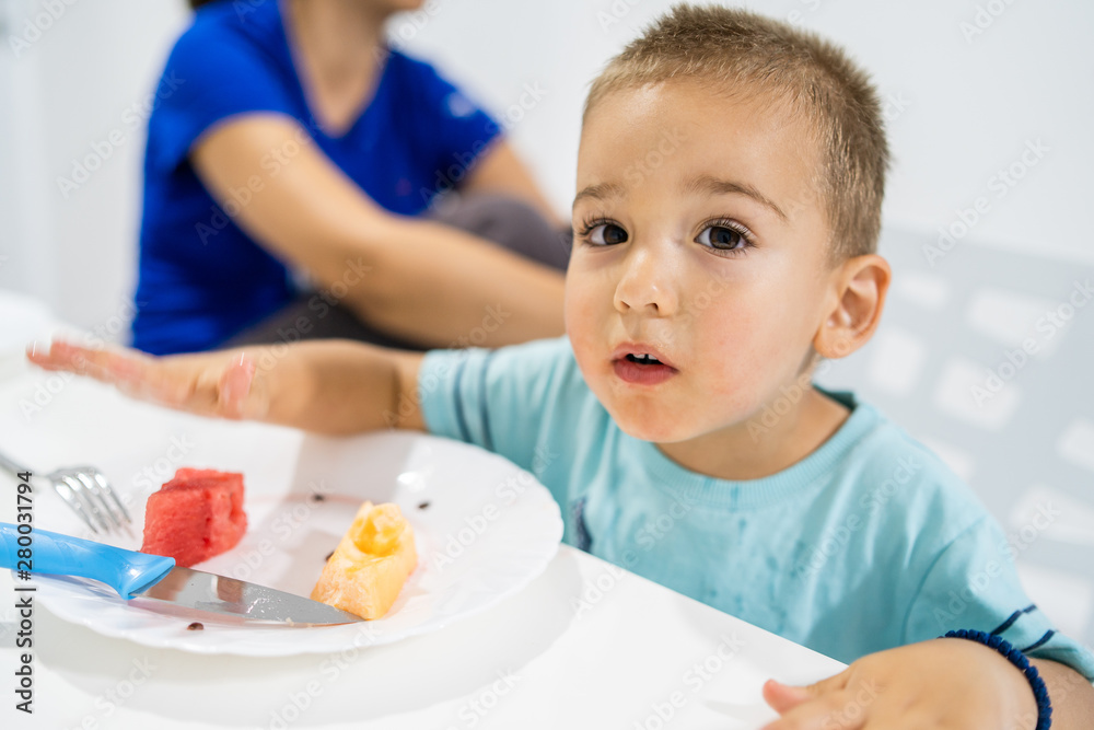 Little boy eating watermelon by the table at home Little boy eating watermelon by the table at home