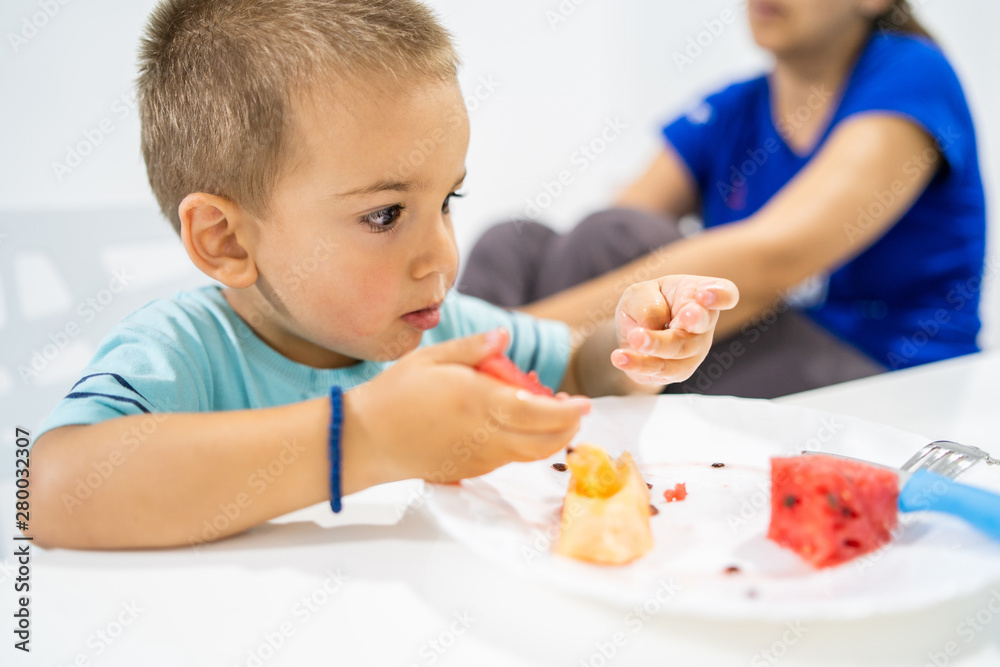 Little boy eating watermelon by the table at home Little boy eating watermelon by the table at home