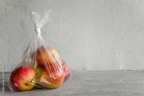 Fresh natural fruit in plastic bag on grey background. The concept of harm of food storage in artificial packages.