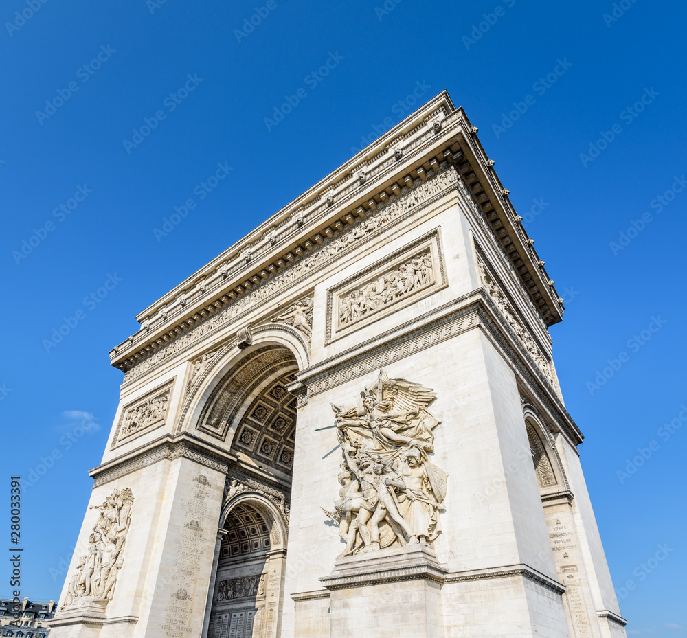 Three-quarter view of the eastern facade of the Arc de Triomphe in Paris, France, illuminated by the morning sunlight under a blue sky.