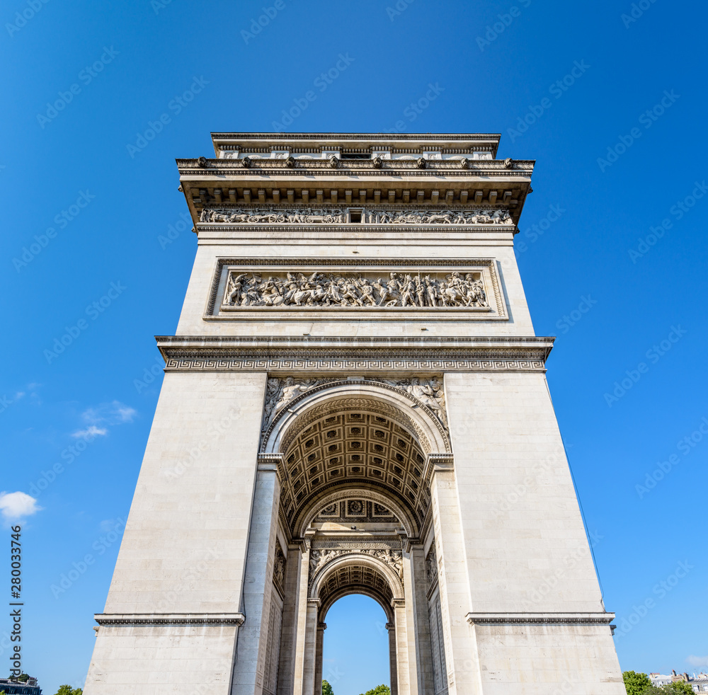 Front view of the northern pillar of the Arc de Triomphe in Paris, France, illuminated by the morning sunlight under a blue sky.