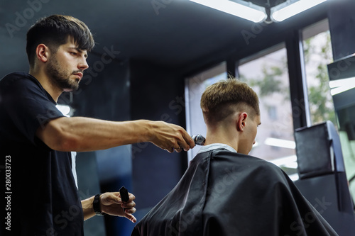 Male haircut with electric razor. Barber makes haircut for client at the barber shop by using hairclipper. Man hairdressing with electric shaver.