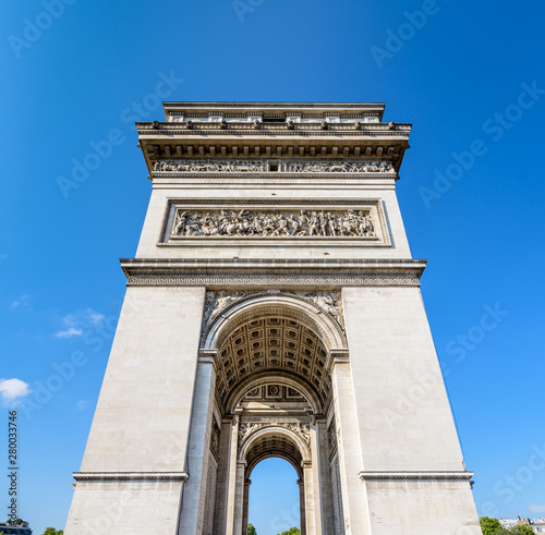 Front view of the northern pillar of the Arc de Triomphe in Paris, France, illuminated by the morning sunlight under a blue sky.