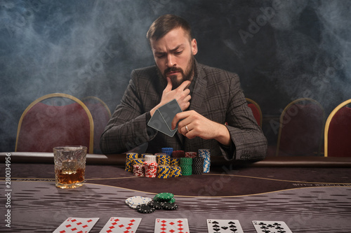 Quadro su tela Handsome bearded man is playing poker sitting at the table in casino