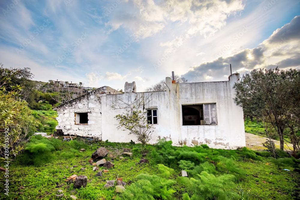 Old abandoned ruin white village house in a rural meadow field.