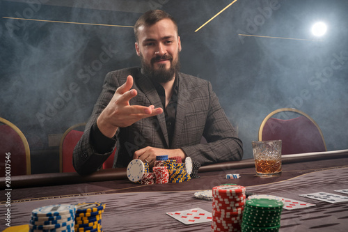 Obraz na płótnie Handsome bearded man is playing poker sitting at the table in casino