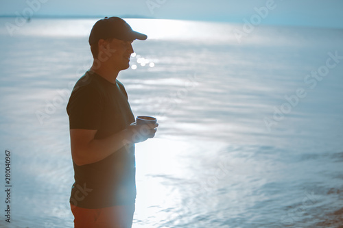 man with travel cup drinking near at sea beach walking in water