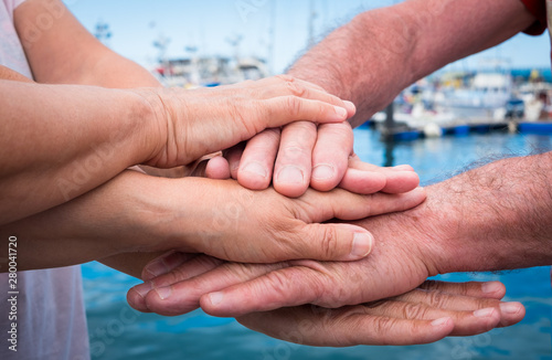 hands of three people who join forces to reach a goal. Union and complicity. Caucasian people. Aged over 65 years. Ocean water on background