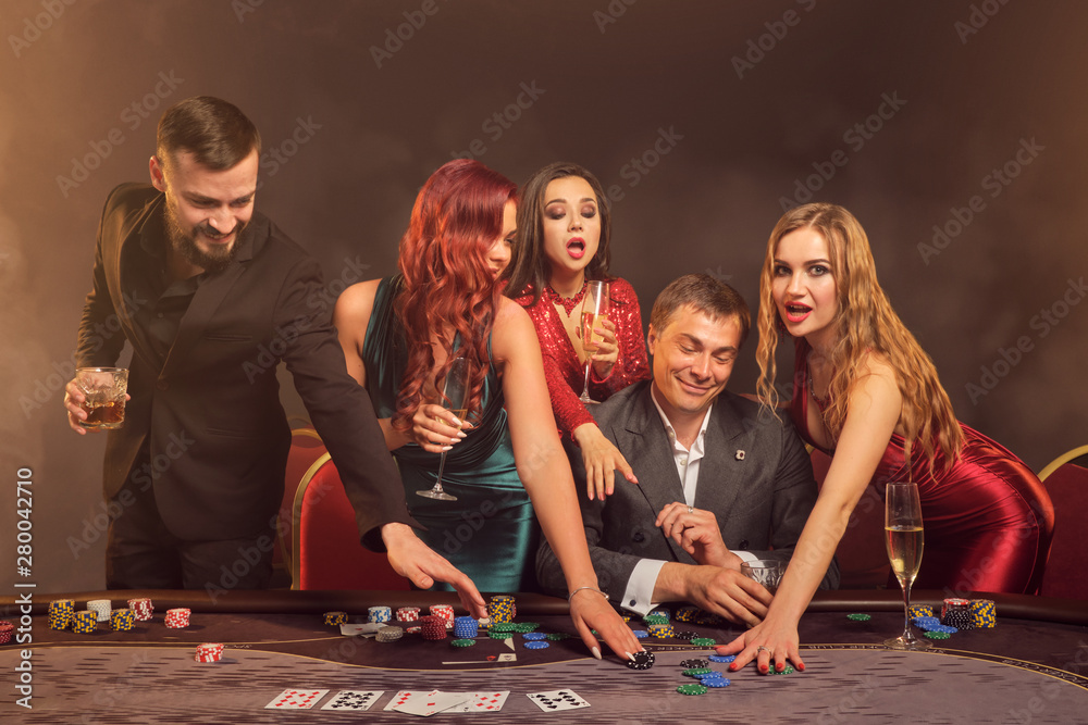 Group of a young wealthy friends are playing poker at a casino. - obrazy, fototapety, plakaty 