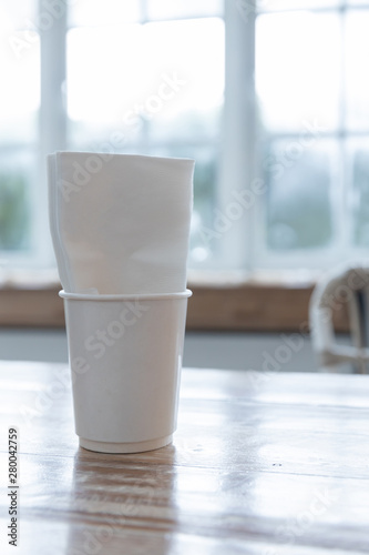 closeup of white takeaway paper cup with tissue napkin on wooden table.